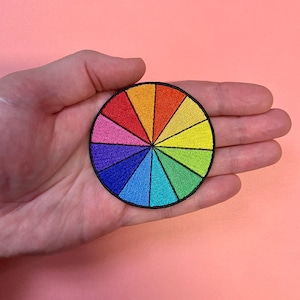 May include: A colourful embroidered patch in the shape of a circle, depicting a colour wheel with 12 sections of different colours.