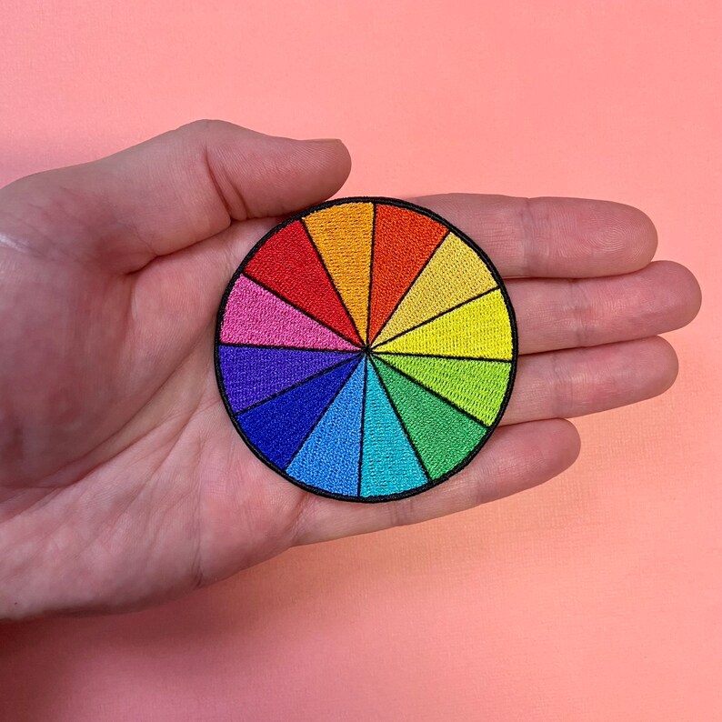 May include: A colorful embroidered patch in the shape of a circle, depicting a color wheel with 12 sections of different colors.