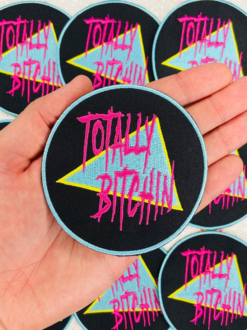 May include: A black and blue embroidered patch with a yellow triangle and the text "Totally BitchiN" in pink.