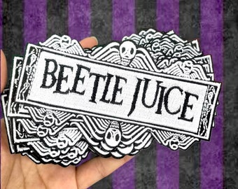 May include: A pile of white and black embroidered patches with the text "BEETLEJUICE" in a decorative frame. The patches feature skull and wing designs. The background is a striped pattern of purple and black.