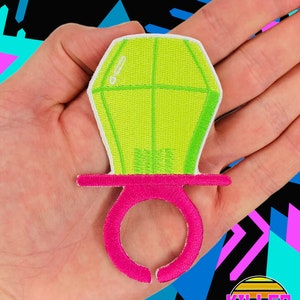 May include: A green and pink fabric patch shaped like a ring pop candy. The ring pop is a popular candy with a hard candy center and a ring that can be worn on the finger.