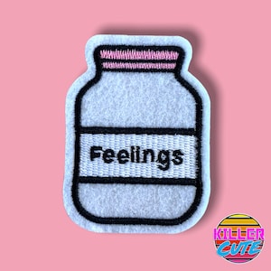 May include: White felt patch with a black outline of a jar with a pink lid. The jar has a white label with the word "Feelings" in black text.