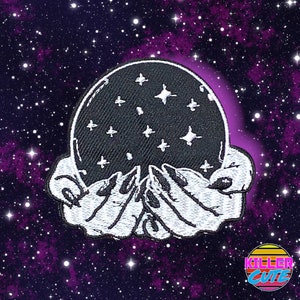 May include: An embroidered patch depicting two hands holding a black crystal ball with white stars, set against a purple and black starry background.