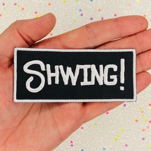 May include: Black iron-on patch with white embroidered text that reads "SHWING!"