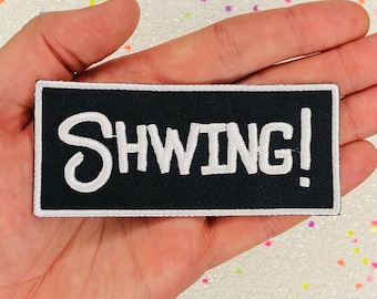 May include: Black iron-on patch with white embroidered text that reads "SHWING!"