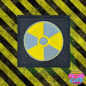 May include: A black fabric patch with a yellow and grey embroidered radiation symbol.