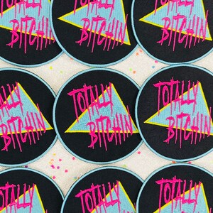 May include: Nine black and blue round iron-on patches with a yellow triangle and the text "Totally Bitchin'" in pink lettering.