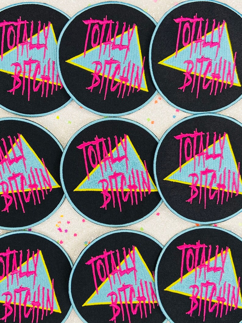 May include: Nine black and blue round iron-on patches with a yellow triangle and the text "Totally Bitchin'" in pink lettering.