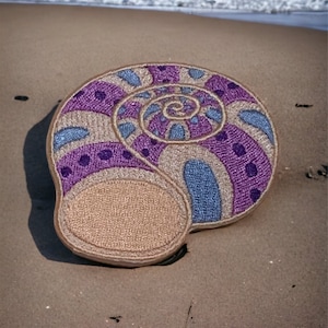May include: A purple and blue seashell with a spiral pattern, lying on a sandy beach.
