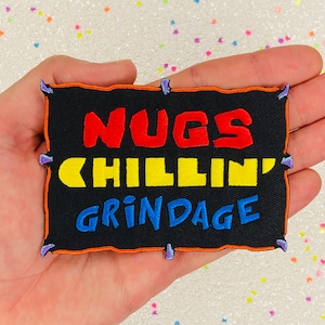 May include: A black embroidered patch with an orange border. The patch says "NUGS CHILLIN' GRINDAGE" in red, yellow, and blue lettering.