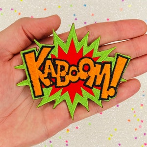 May include: Embroidered patch featuring the word "KABOOM!" in orange, outlined in black, on a red and green burst design. The patch is a comic book style design.