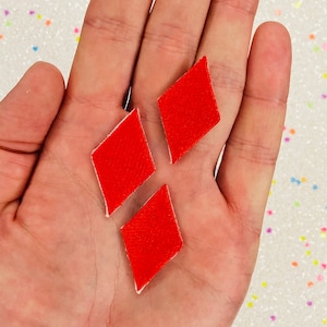 May include: Three red felt diamond shapes on a hand. The diamonds are approximately 2.5 cm in size.