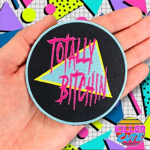 May include: A black and blue round patch with a pink triangle and the text "Totally Bitchen" in pink.