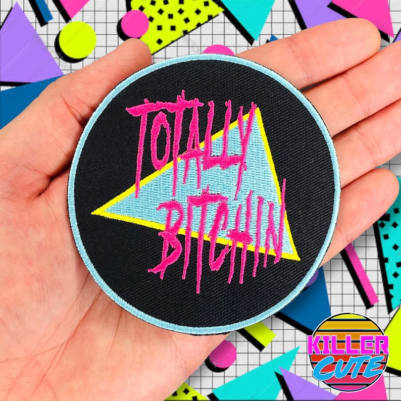 May include: A black and blue round patch with a pink triangle and the text "Totally Bitchen" in pink.
