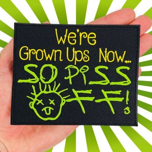 May include: Black iron-on patch with yellow and green embroidery. The patch says "We're Grown Ups Now... So Piss Off!" with a stick figure drawing of a person with a tongue sticking out and an X for eyes.