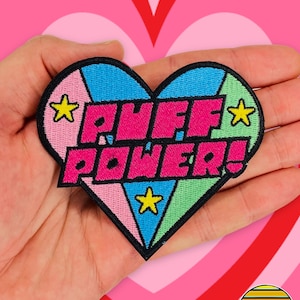 May include: A pink, blue and green heart-shaped embroidered patch with the text "PUFF POWER!" and yellow stars.