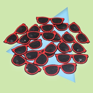 May include: A pile of red and black sequin sunglasses patches. The patches are made of black sequins with a red border.
