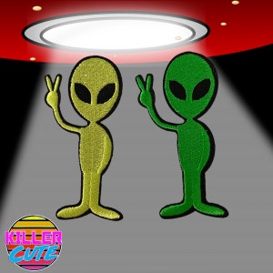 May include: Two embroidered iron-on patches of aliens with peace signs. The alien on the left is yellow and the alien on the right is green.