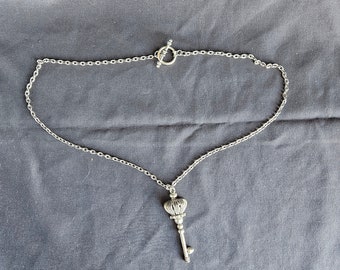 May include: A silver key necklace with a detailed key pendant and a silver chain. The chain has a lobster clasp closure.