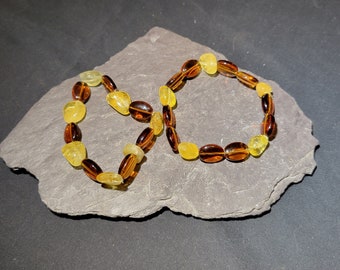 May include: Two amber bracelets with yellow and brown beads. The bracelets are on a gray slate surface.