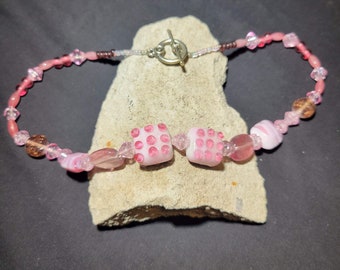 May include: Pink and white beaded necklace with a silver clasp and two pink dice-shaped beads.