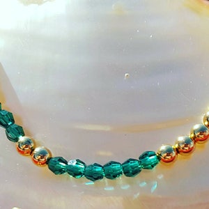 May include: A gold chain bracelet with alternating green glass beads and gold beads.