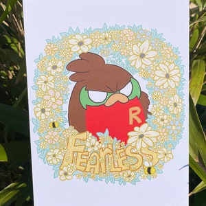 Può includere: Un'illustrazione di un cartone animato di un uccello rosso con una maschera verde e la lettera "R" sul petto. L'uccello è circondato da una ghirlanda di fiori gialli e bianchi con accenti blu e verdi. La parola "FEARLESS" è scritta in lettere gialle sotto l'uccello.