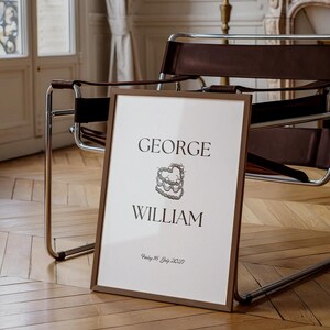 Può includere: Una stampa incorniciata con i nomi "GEORGE WILLIAM" e un'illustrazione di torta stilizzata. La data "Friday 15 July 2027" è stampata sotto i nomi.