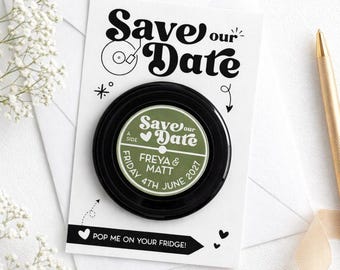 May include: A black magnet in the shape of a vinyl record, with the words "Save our Date" in a retro font. The center label reads "FREYA & MATT, FRIDAY 4TH JUNE 2027." Text at the bottom says "POP ME ON YOUR FRIDGE!"