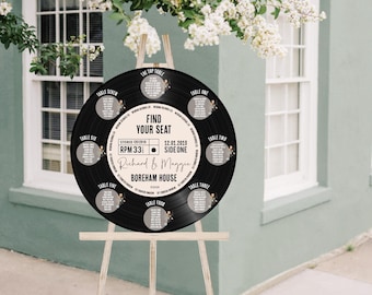 May include: A black vinyl record seating chart for a wedding, displayed on a wooden easel. The chart features the text "Find Your Seat" and table assignments. The names "Richard & Maggie" and "Boreham House" are also visible.