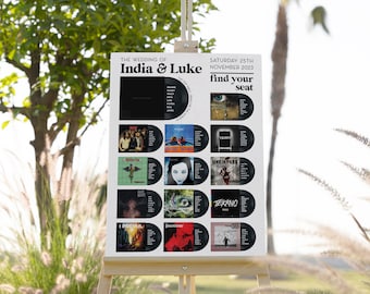 May include: A white wedding seating chart with a black and white record album theme. The chart is titled "The Wedding of India & Luke" and "Saturday 25th November 2023". The chart has the words "find your seat" in a large font.