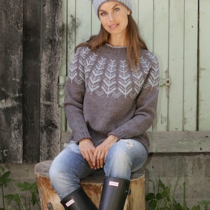 May include: A gray sweater and beanie set with a light blue leaf pattern. The sweater is paired with blue jeans and black rain boots. The woman is sitting on a tree stump.