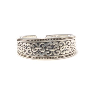 Puede incluir: Un brazalete de plata con un diseño intrincado y ornamentado. El brazalete está hecho de metal liso y pulido y tiene una forma ligeramente curvada.