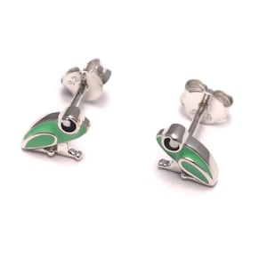 May include: A pair of silver frog stud earrings with green enamel detailing. The earrings feature a detailed frog design with black eyes and are set against a white background. The earrings are small and delicate.