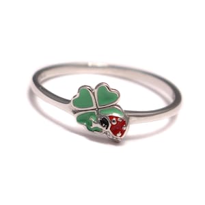 May include: A silver ring with a green four-leaf clover and a red ladybug charm.