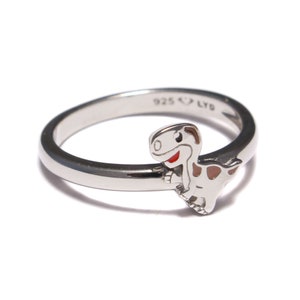 Könnte beinhalten: Ein silberner Ring mit einem Cartoon-Dinosaurier-Design. Der Dinosaurier ist weiß mit roten und braunen Akzenten. Der Ring ist mit "925 LYD" gekennzeichnet.