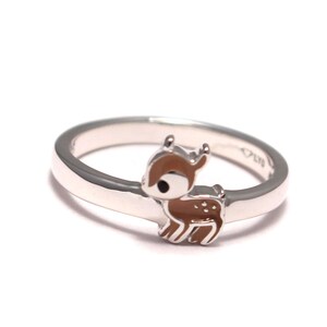 Può includere: Un anello d'argento con un ciondolo a forma di cervo in smalto marrone. Il cervo ha occhi neri e dettagli bianchi.