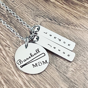 May include: Silver necklace with a round pendant that says "Baseball Mom" with a baseball and bat graphic. The necklace also has three silver charms with the letters "L", "J & A", and "S & D" engraved on them.