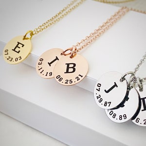 May include: Three gold, rose gold, and silver necklaces with personalized initial and date charms. The gold necklace has a charm with the letter "E" and the date "07.23.03". The rose gold necklace has a charm with the letter "I" and the date "03.11.19" and a charm with the letter "B" and the date "06.25.21". The silver necklace has three charms with the letters "J", "T", and the dates "07.29.87", "08.08.89", and "06.20.91".