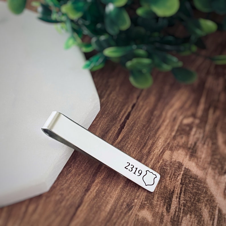 May include: Silver tie bar with a shield design and the number 2319 engraved on it.