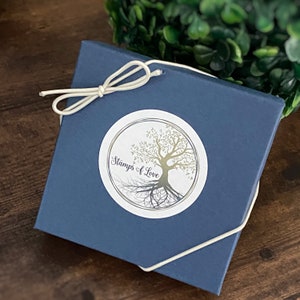Qr code keychain packaged in a square blue jewelry box from stamps of love closed with a white bow stretch loop.