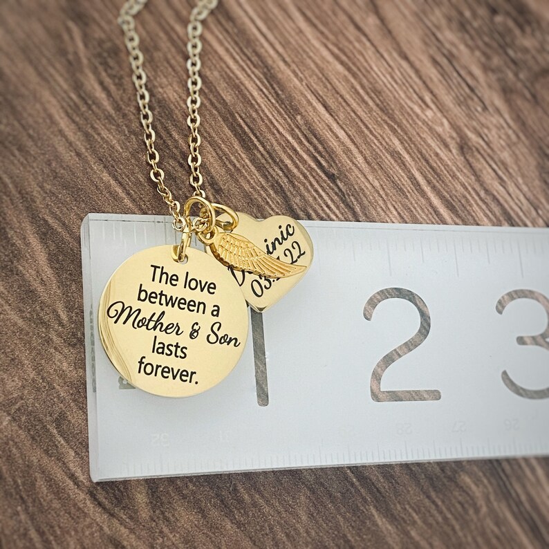 Puede incluir: Collar de oro con un colgante redondo que dice "El amor entre una madre y un hijo dura para siempre." y un colgante en forma de coraz&oacute;n con un ala de &aacute;ngel y la inscripci&oacute;n "Dominic 03.22".