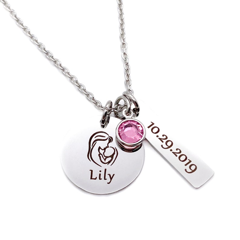 Mom Silver Charm Necklace with a 1 inch round pendant engraved with a mom and baby image and the daughter's name Lily. next charm is a pink October birthstone. next charm is a rectangle tag engraved with the date 10.29.19.