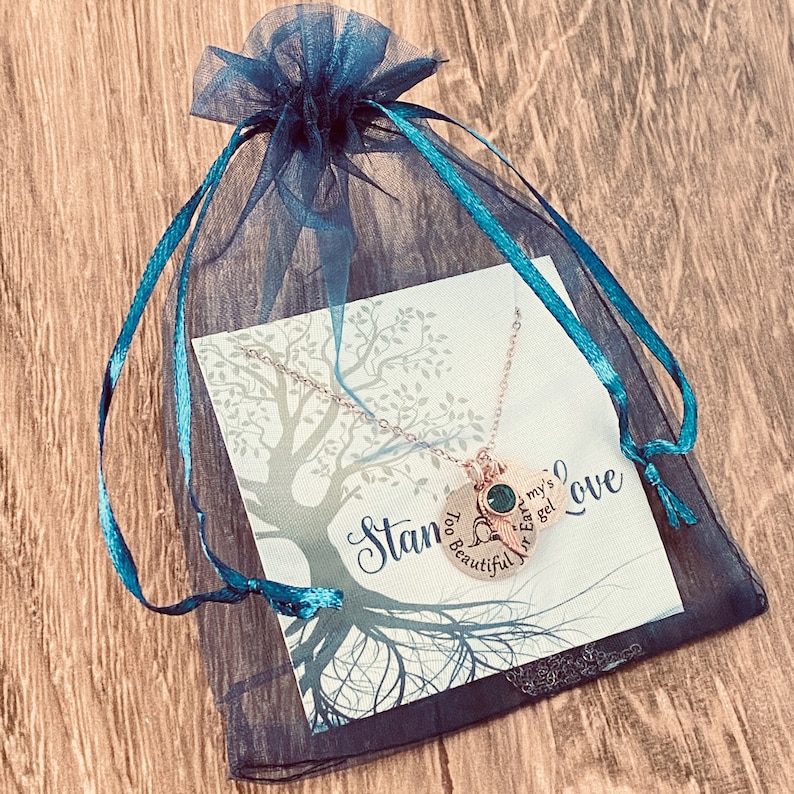 Puede incluir: Un collar de oro con dos dijes, uno con una piedra verde y el texto "Ear my's Angel" y el otro con el texto "Too Beautiful for Love". El collar se muestra en una tarjeta azul y negra con un dise&ntilde;o de &aacute;rbol y el texto "Stan".