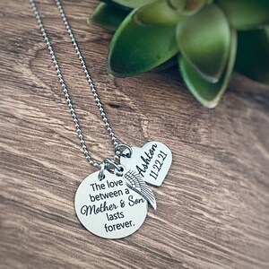 Puede incluir: Collar de plata con dos colgantes. El colgante m&aacute;s grande es redondo y est&aacute; grabado con el texto "The love between a Mother & Son lasts forever." El colgante m&aacute;s peque&ntilde;o es un coraz&oacute;n con el nombre "Ashton" y la fecha "11.22.21" grabados.