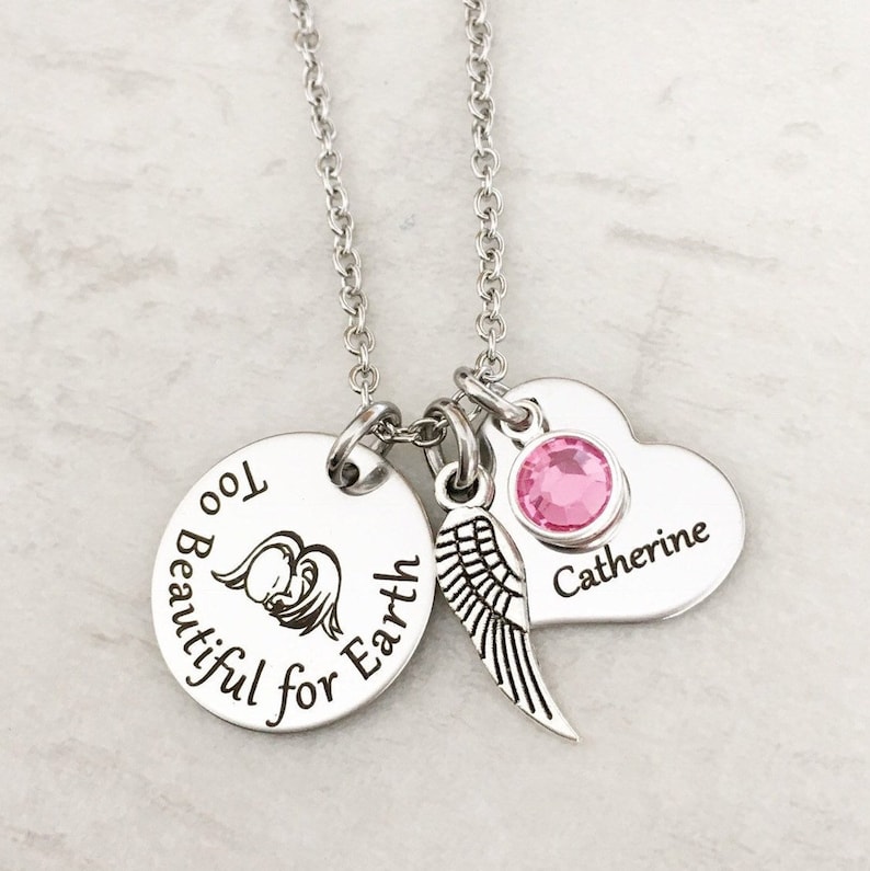 Puede incluir: Collar de plata con un dije redondo que dice "Too Beautiful for Earth" con un peque&ntilde;o &aacute;ngel y alas. El collar tambi&eacute;n tiene un dije en forma de coraz&oacute;n con el nombre "Catherine" y un cristal rosa.