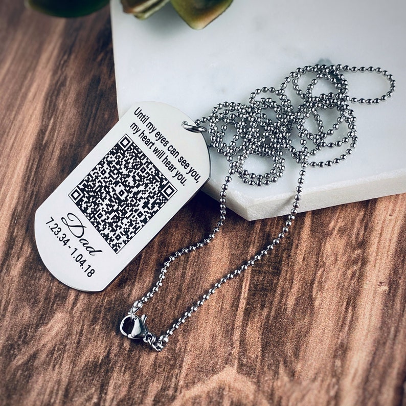 Qr Code with Dad's voice engraved on a dog tag attached to a 30 inch ball chain to wear as a necklace or rearview mirror accessory. The saying Until my eyes can see you, my heart will hear you, the qr code, name Dad, and dates 7.23.34 - 1.4.18