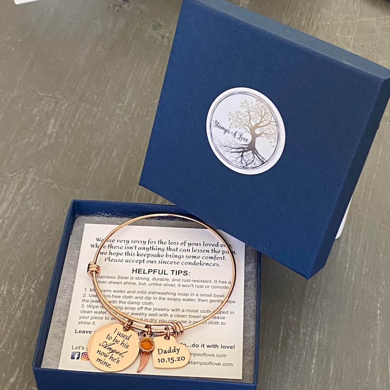 May include: A gold-toned bracelet with charms that say "I used to be his Angel now he's mine" and "Daddy 10.15.20". The bracelet is in a blue box with a white logo that says "Stamp's A Love".