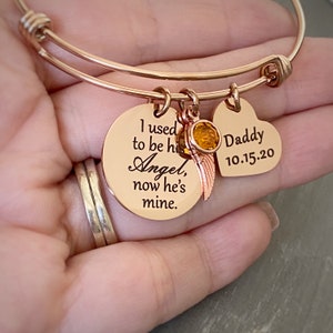 May include: Rose gold bangle bracelet with two charms. One charm is a round disc with the text "I used to be his Angel, now he's mine." The other charm is a heart with the text "Daddy 10.15.20".