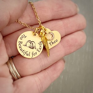 Puede incluir: Collar de oro con un colgante redondo que dice "Too Beautiful for Earth" con una peque&ntilde;a imagen de un beb&eacute; &aacute;ngel. El collar tambi&eacute;n tiene un colgante en forma de coraz&oacute;n con el nombre "Theo" y un peque&ntilde;o amuleto de ala de &aacute;ngel dorado.